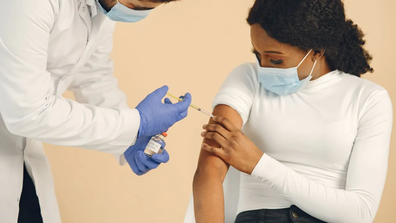 A healthcare professional giving a vaccination to a seated woman, both wearing masks.