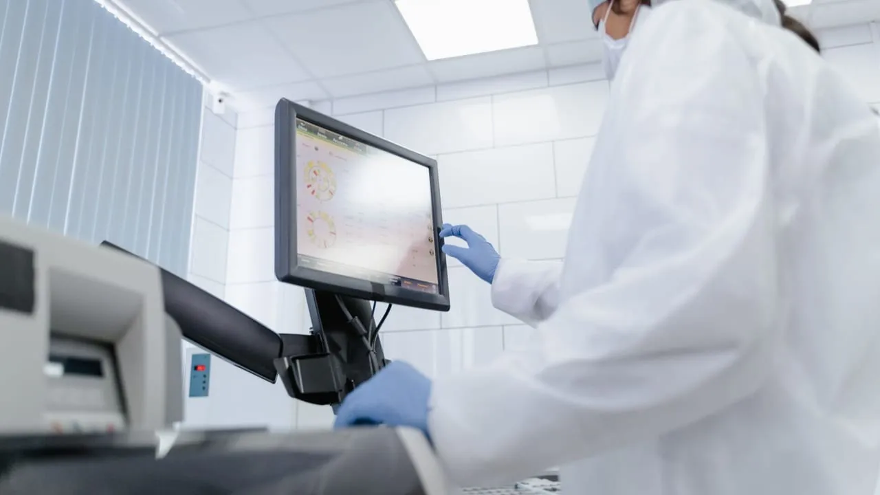 Woman in lab coat using touchscreen monitor in a modern laboratory setting.