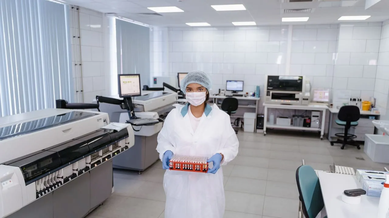 A scientist in protective gear holding test samples in a modern laboratory setting.