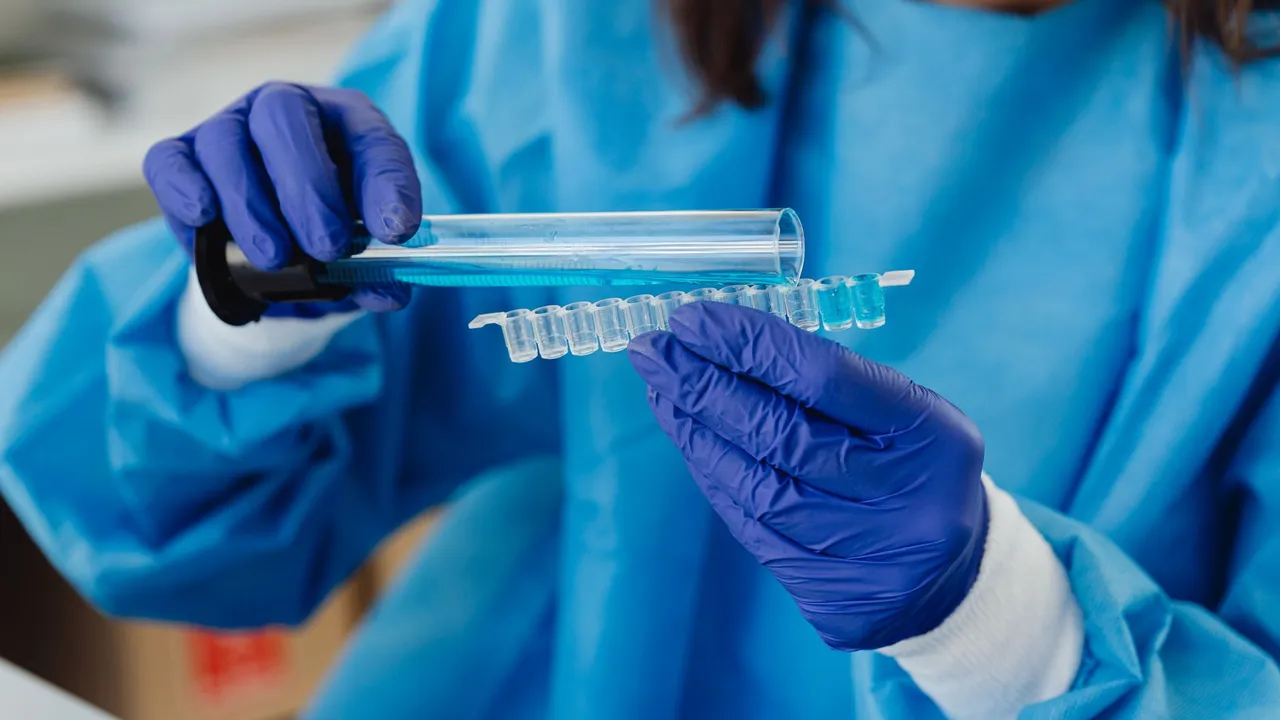 Scientist in blue protective gear conducting laboratory analysis with test tubes and vials.