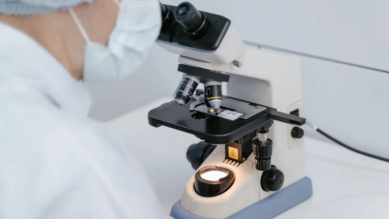 Scientist using a microscope in a laboratory setting, wearing protective gear.