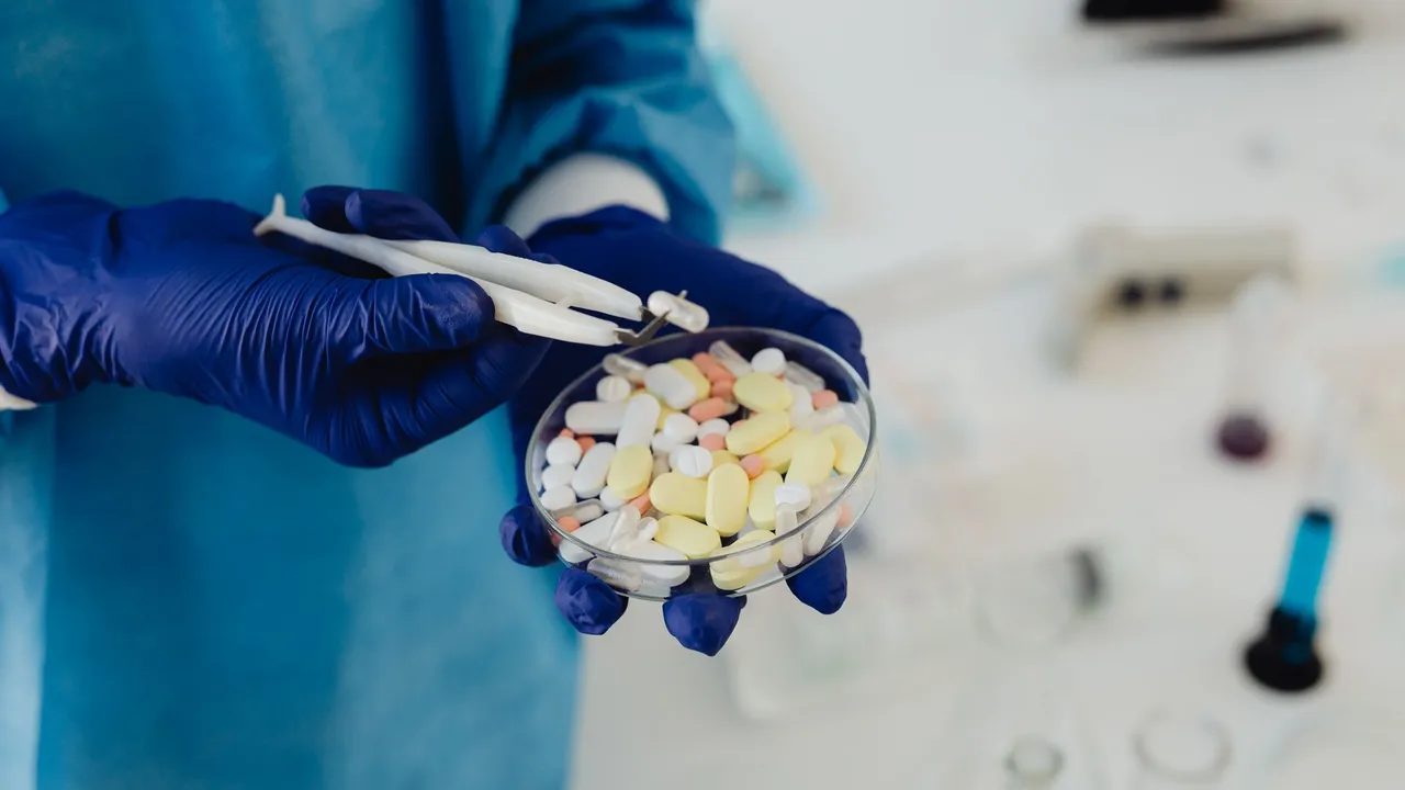 Scientist in gloves using tweezers to handle assorted pills in a petri dish.