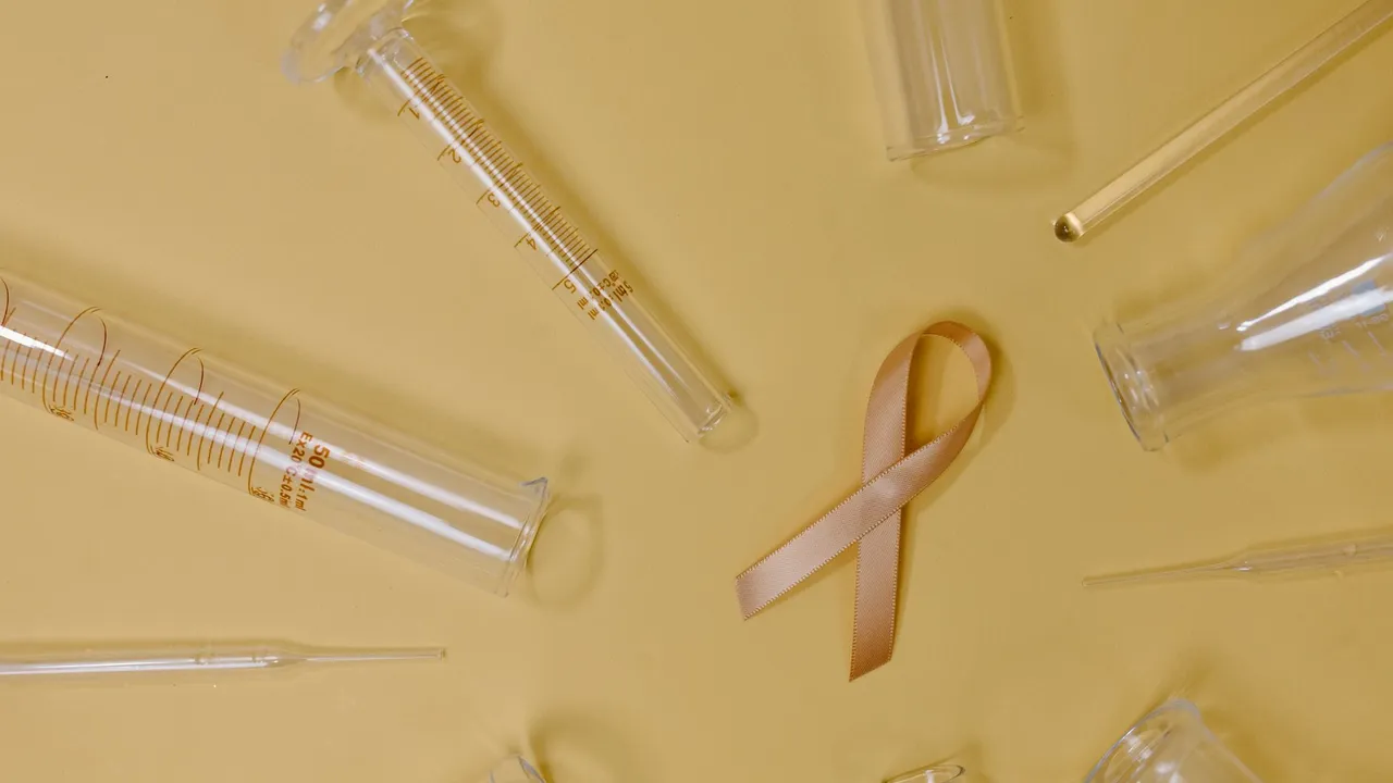 Top view of pink ribbon representing cancer placed on yellow background among glass test tubes and flasks in light studio