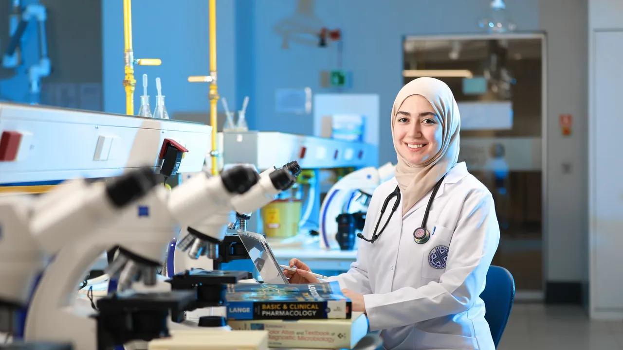 A confident female scientist in a lab coat with a hijab in a modern laboratory with microscopes and textbooks.