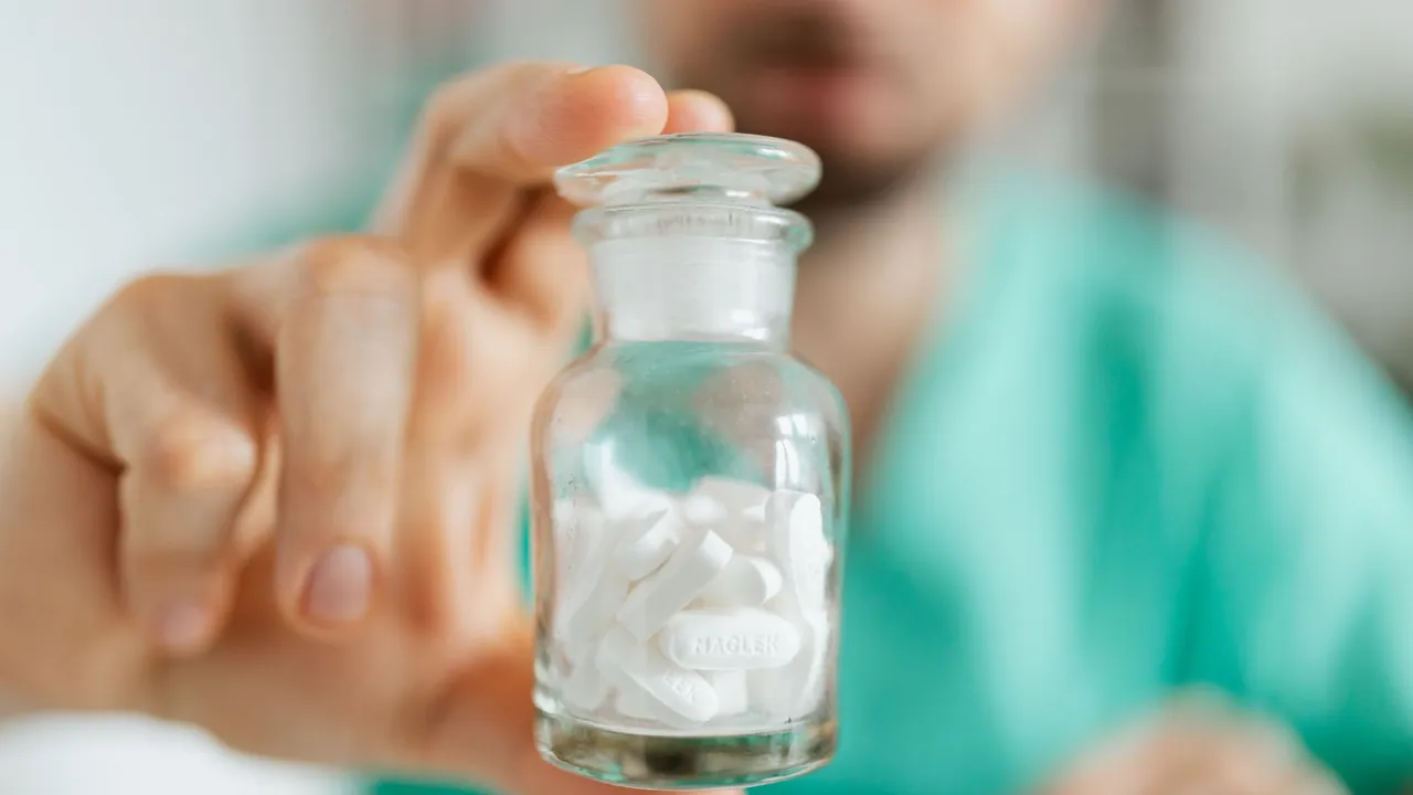 Crop medical worker in uniform holding in hand glass transparent bottle with white pills