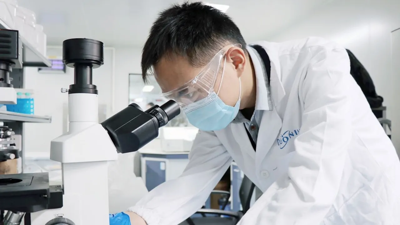 A man in a lab coat and goggles looking through a microscope