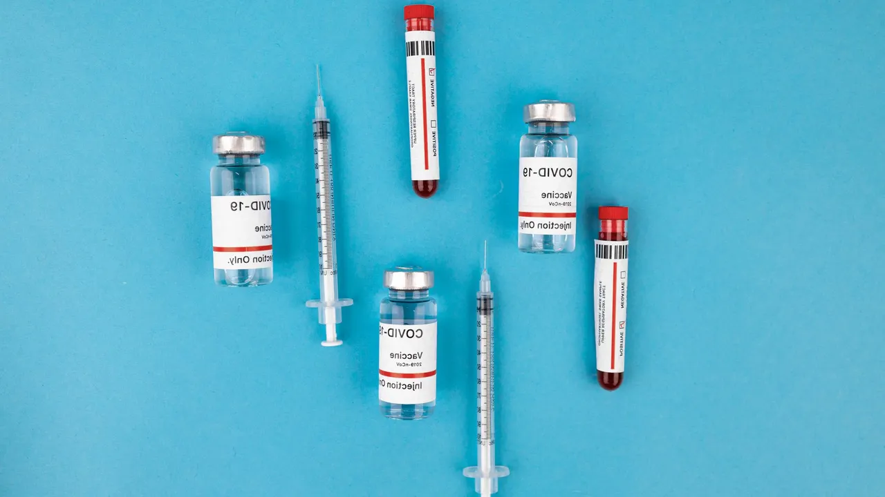 Top view of COVID-19 vaccine vials, syringes, and test tubes on a blue background, representing immunization and protection.