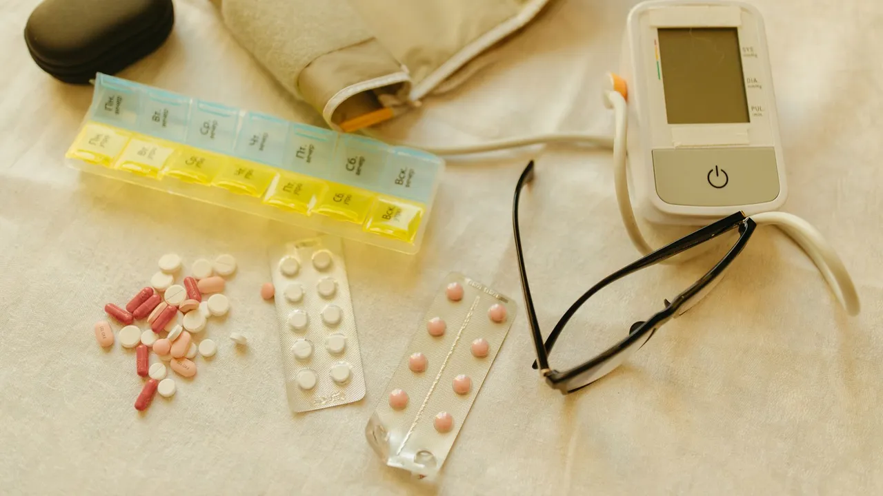 Flat lay image of healthcare essentials including a blood pressure monitor, pills, and eyeglasses on a white surface.