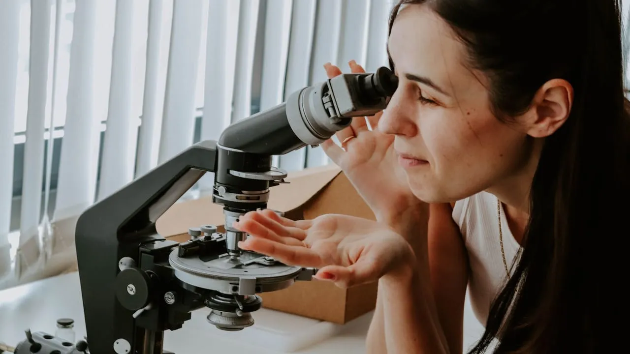 A female researcher examines samples with a microscope in a laboratory setting.