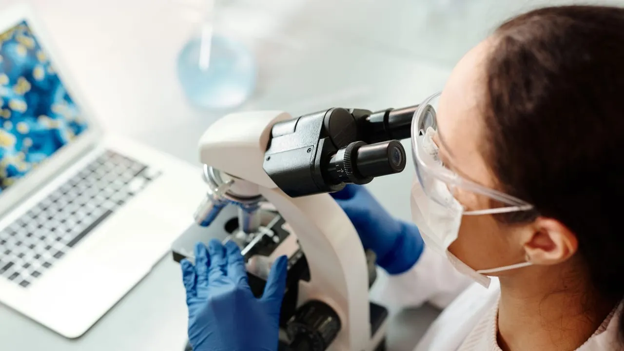 Scientist in protective gear examining samples with microscope in laboratory setting.