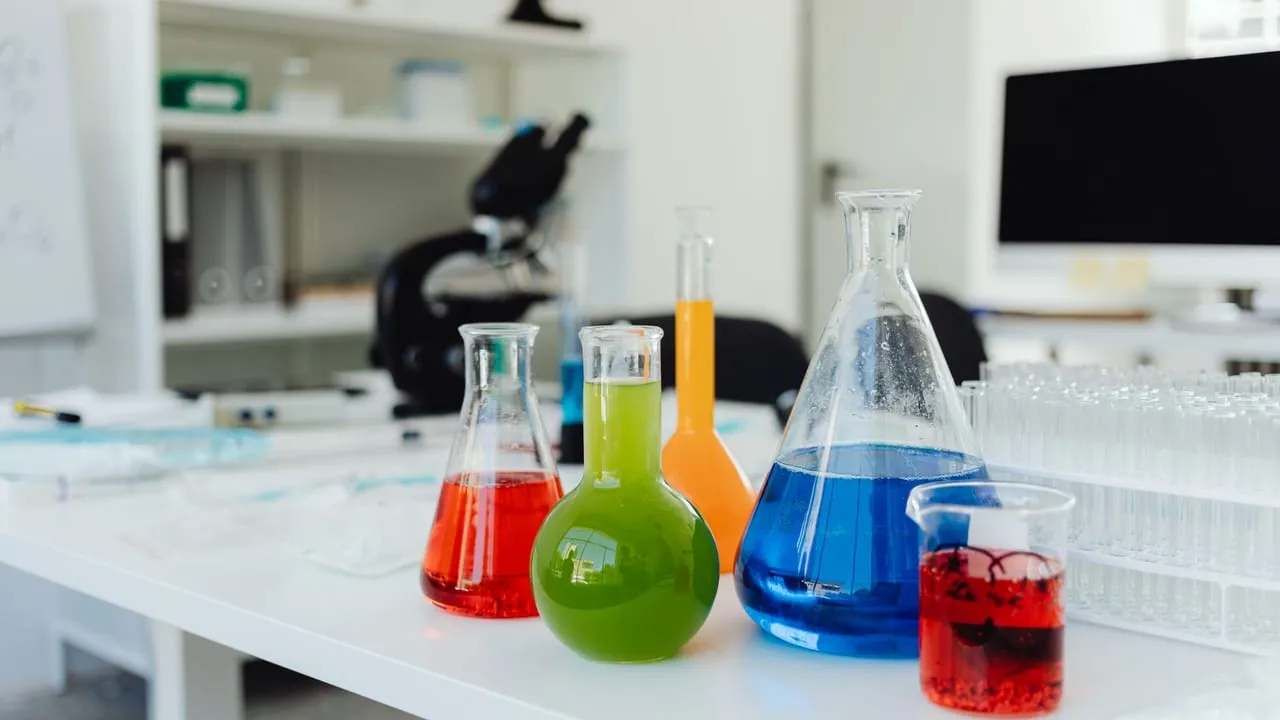 Bright, colorful chemicals in flasks and beakers on a lab table indicating a chemistry experiment in progress.