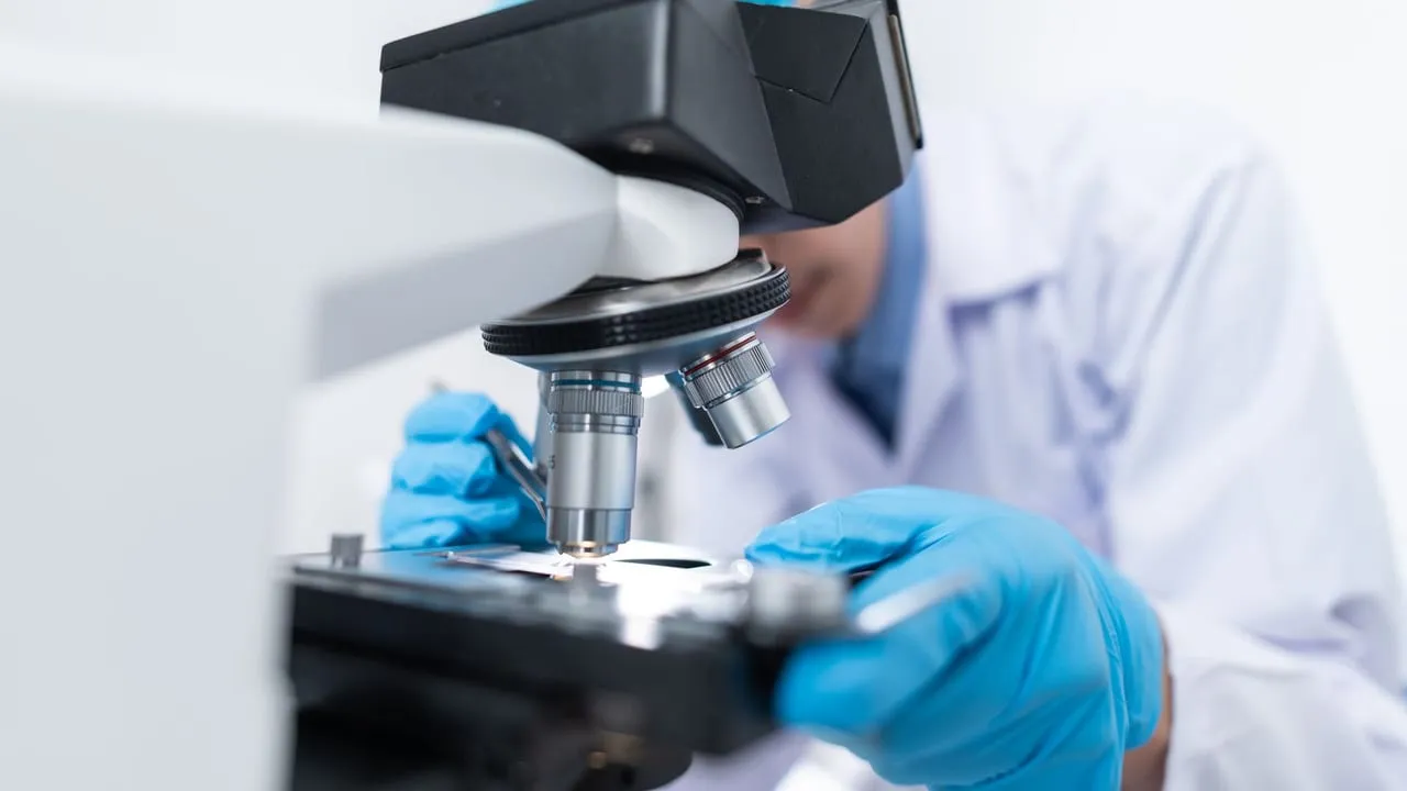 Close-up of a scientist examining samples under a microscope in a lab setting.