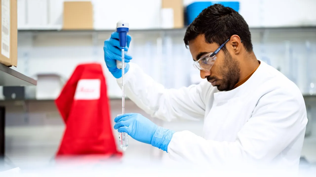 A focused scientist holding a pipette in a laboratory environment.