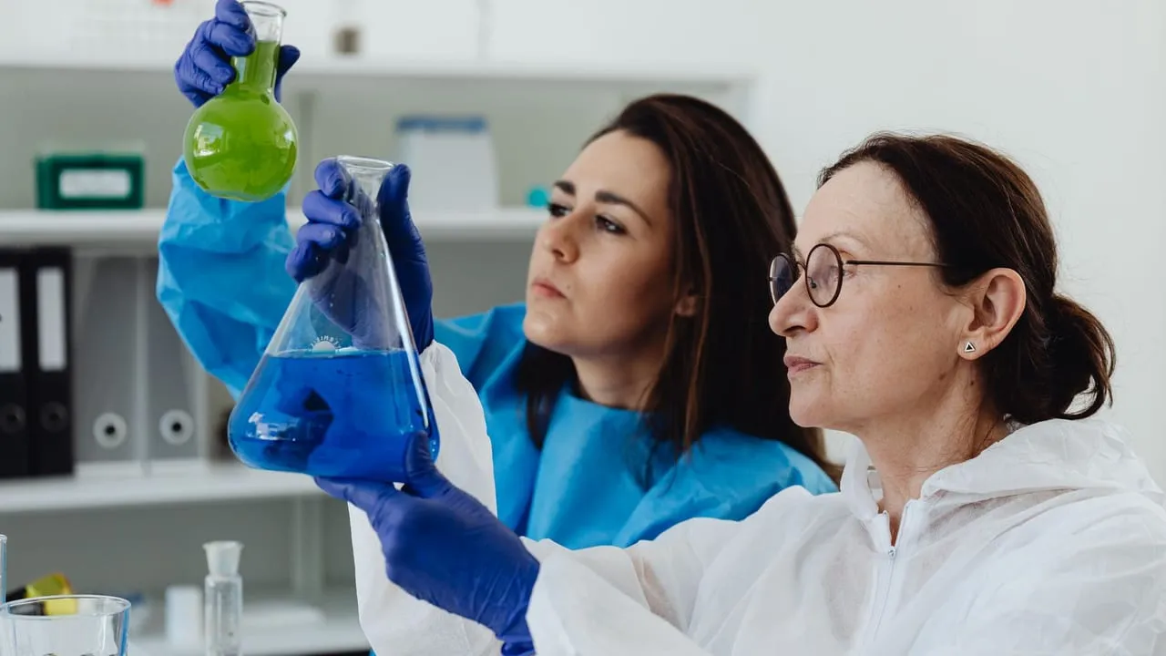 Two female scientists examine colored liquids in a lab setting, showcasing scientific research.