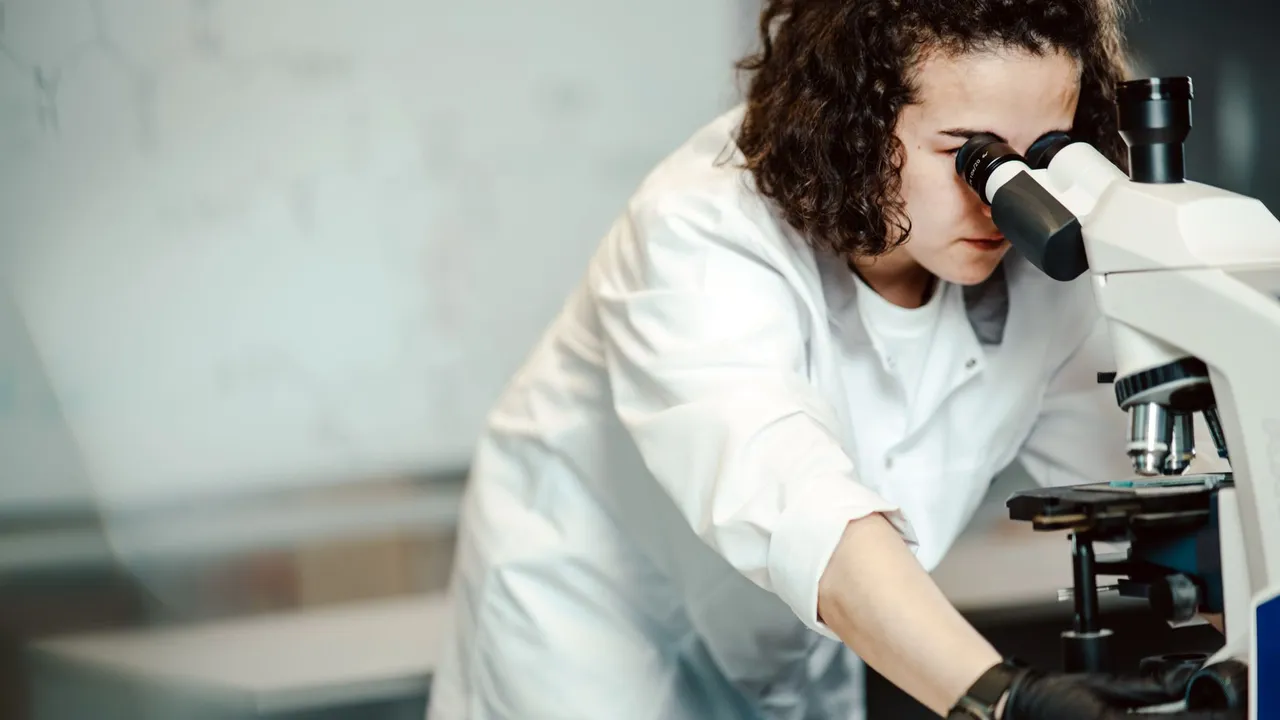 Close-up of a female scientist using a microscope in a laboratory setting, focusing on scientific research.