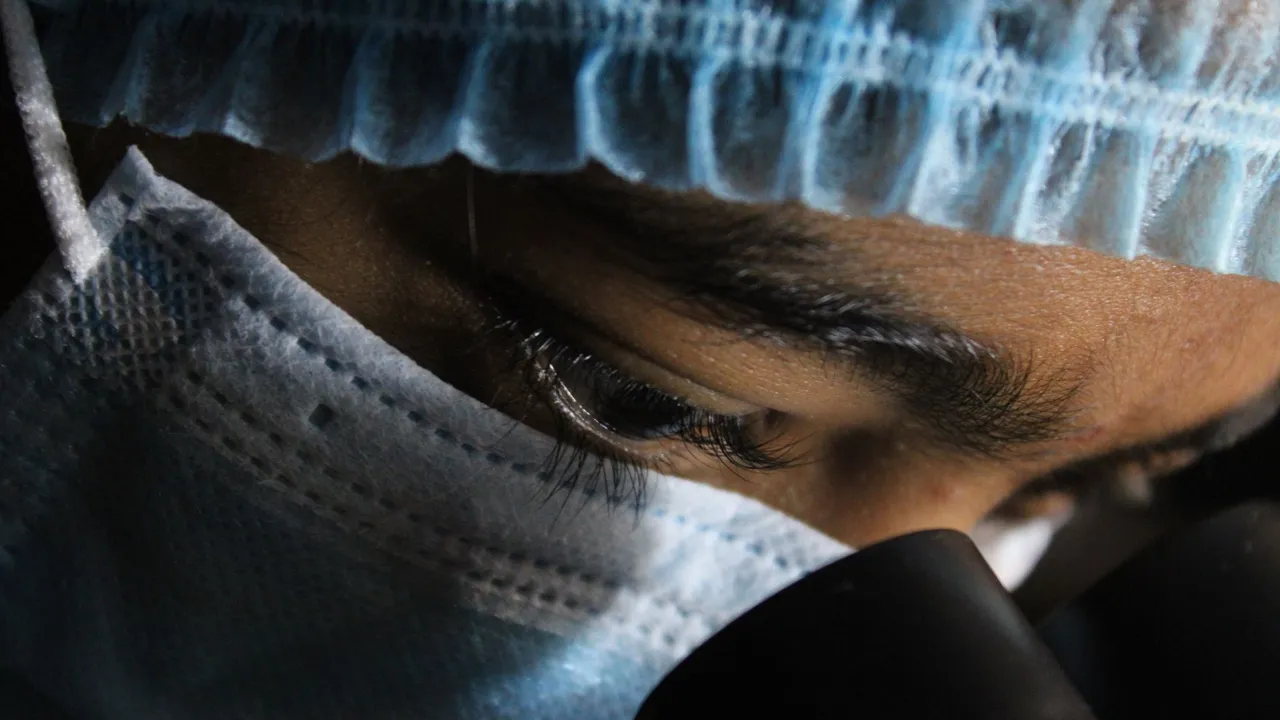 A scientist in protective gear intensely looking through a microscope.