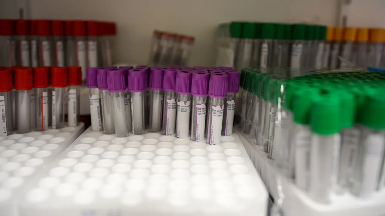 Close-up of labeled blood collection tubes in a laboratory with red, purple, and green caps.