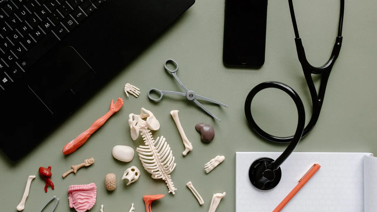 Top view of medical tools, stethoscope, skeleton parts, and laptop on a desk.