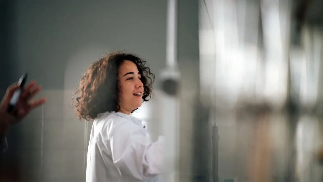 A young female scientist with curly hair in a lab coat working in a laboratory setting.