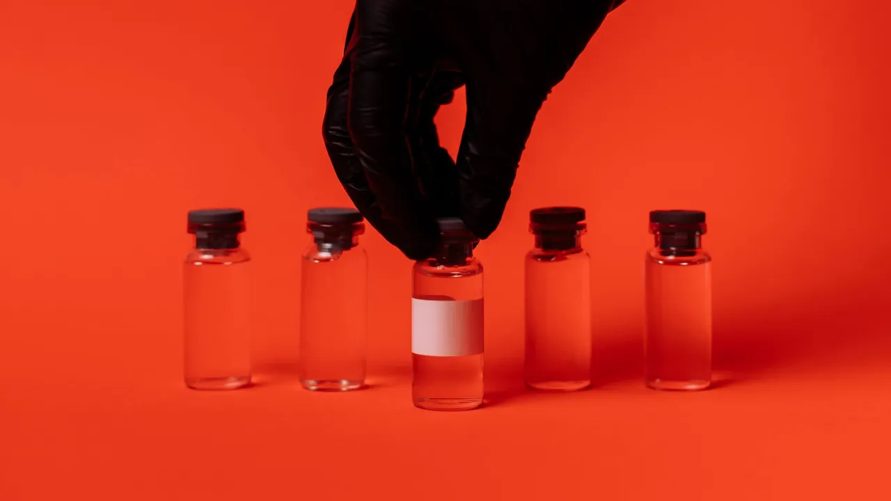Person wearing black glove grabbing a vaccine vial against a bright red backdrop.