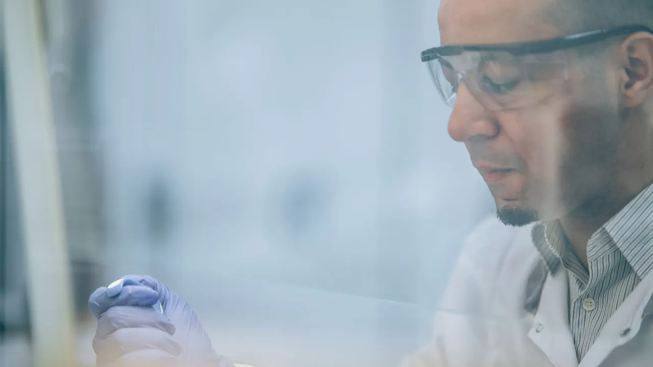 Research scientist wearing safety glasses and gloves in a laboratory setting.
