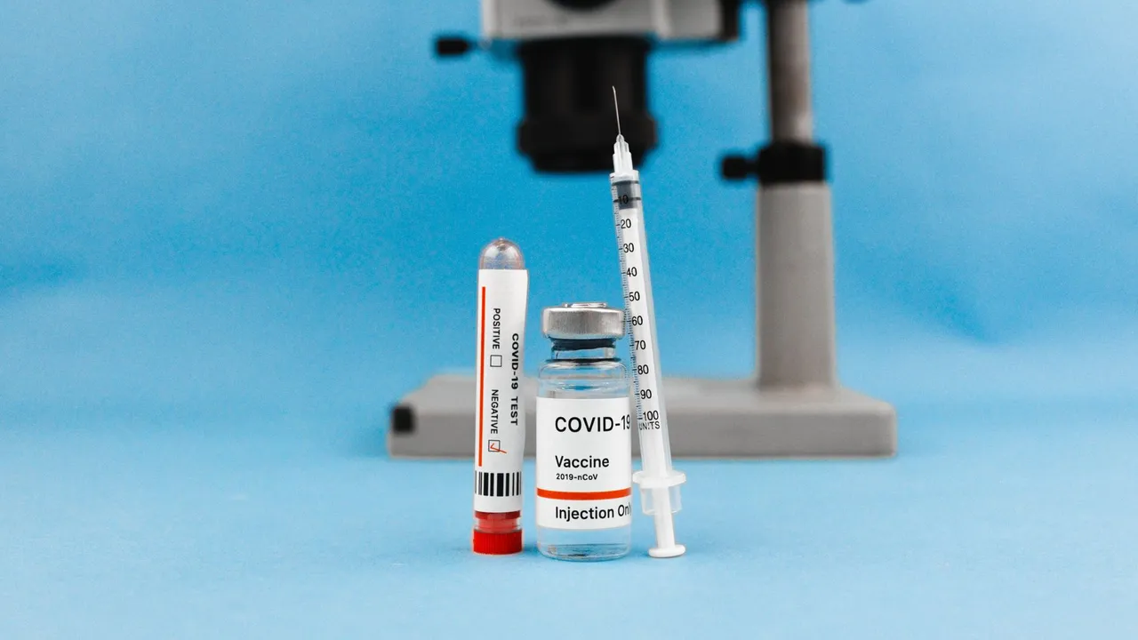 COVID-19 vaccine vial, syringe, test tube, and microscope on blue background, symbolizing research and healthcare.