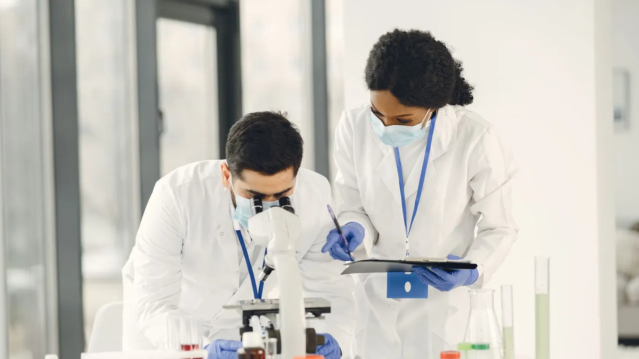 Researchers in lab coats and masks working with microscope and test tubes in a laboratory setting.