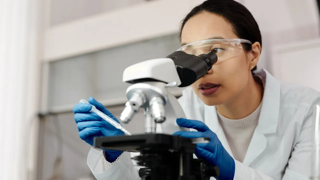 A female scientist examines samples using a microscope in a laboratory setting.