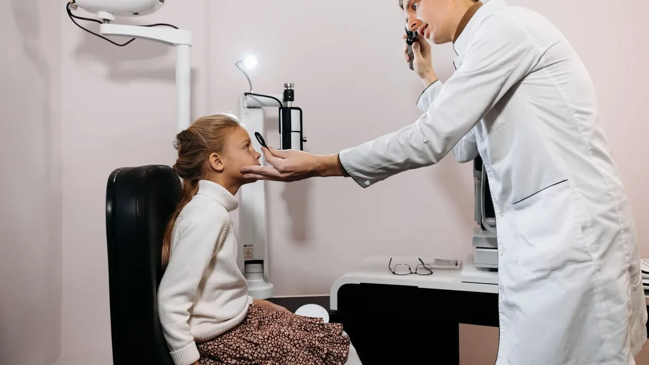 A medical professional performs an eye exam on a young girl in a clinic setting.