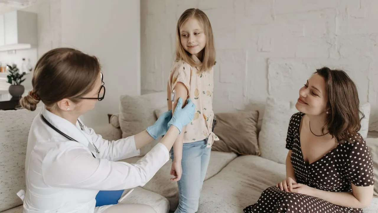 A doctor checks a young girl's arm while her mother watches, emphasizing at-home healthcare.
