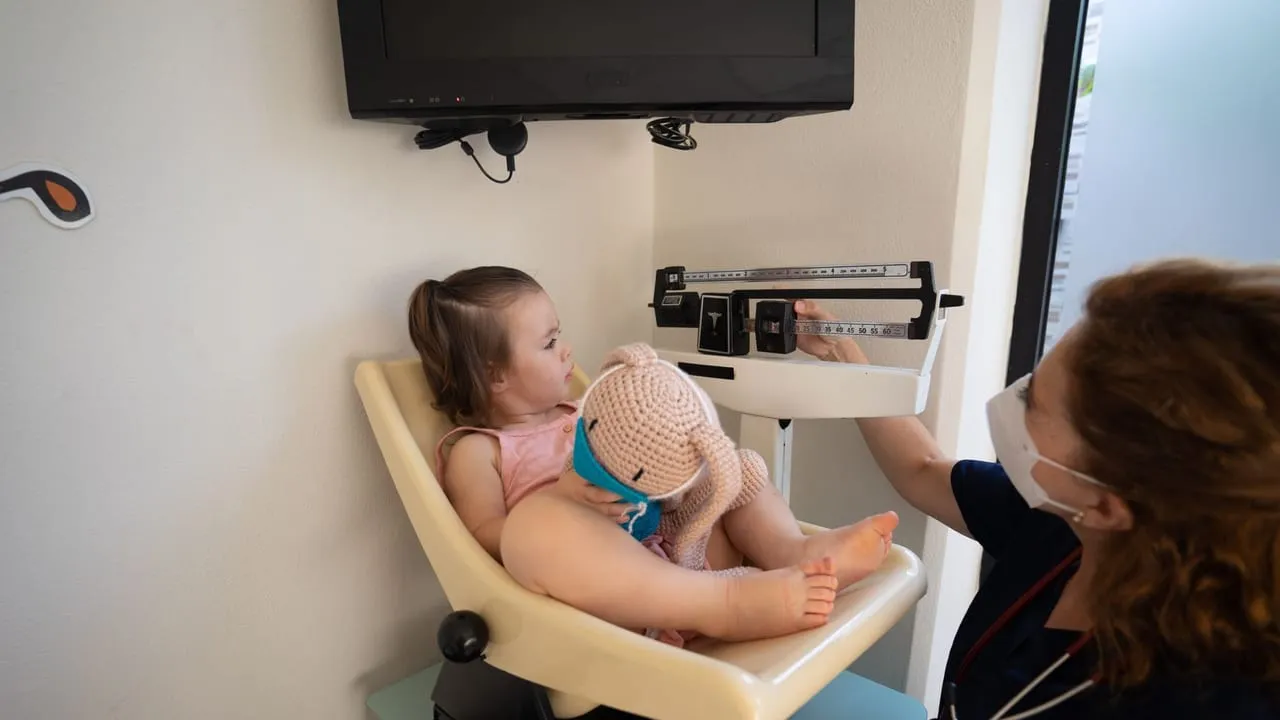 A young girl being weighed by a nurse in a pediatric examination room.