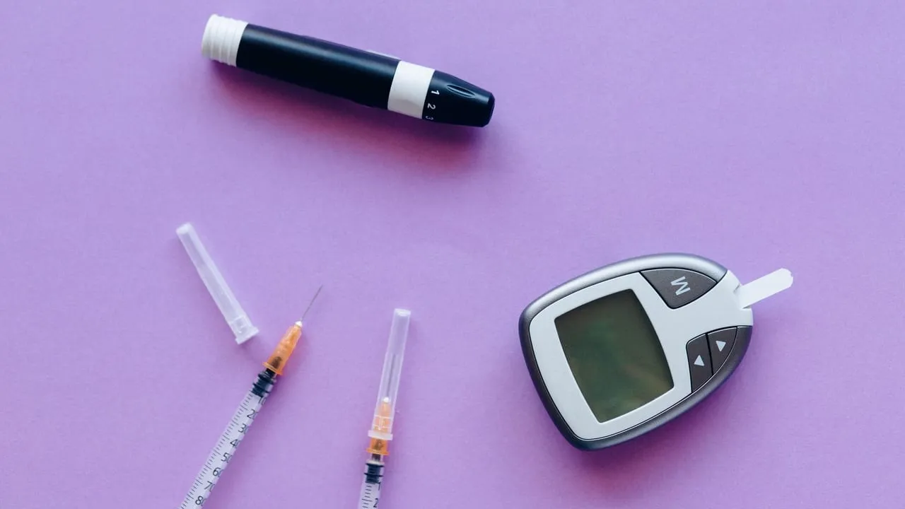 Top view of diabetes management tools including glucose meter and insulin syringes on purple background.