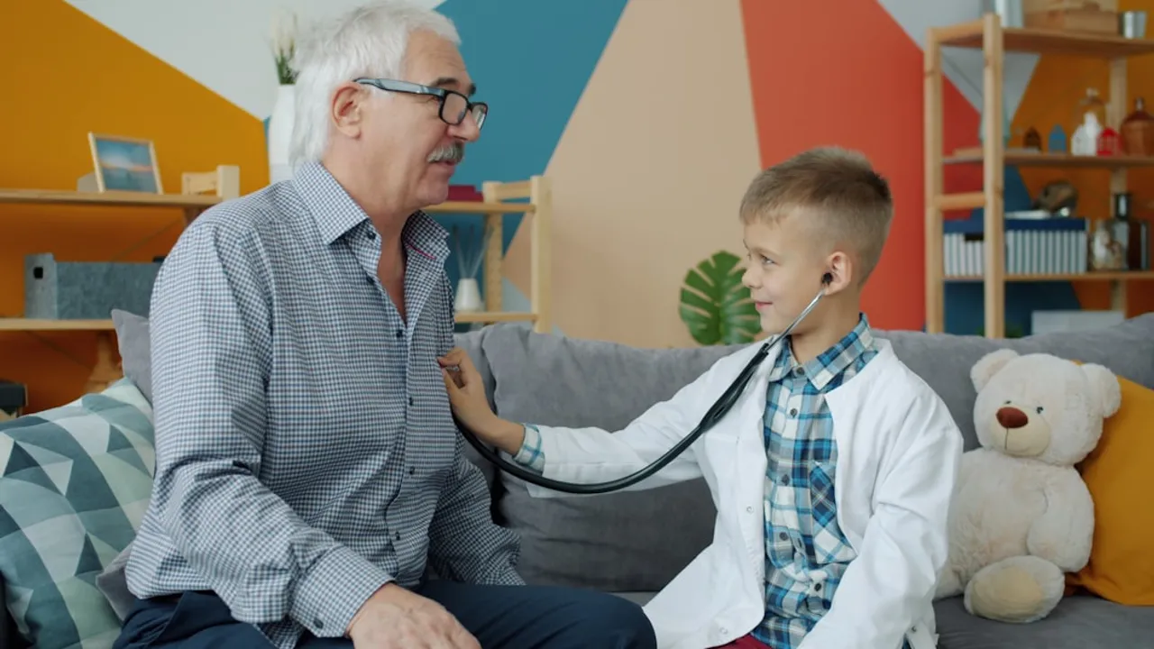 Boy in doctor's coat listens to grandfather's chest