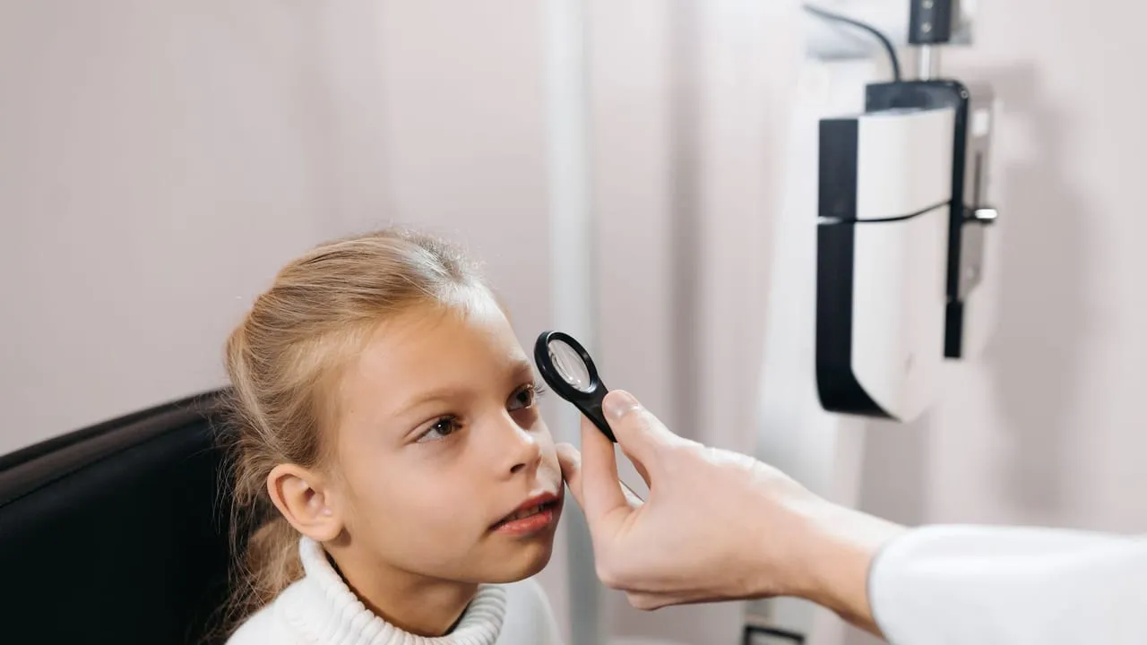 A young girl sitting in an ophthalmologist's office having her eyes examined.