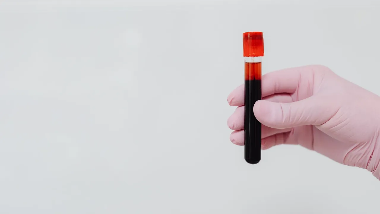 A gloved hand holding a blood sample in a test tube with a white background.