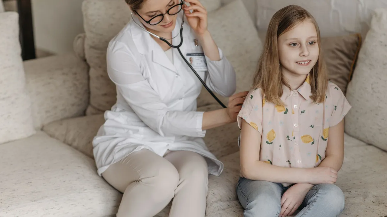 Doctor using a stethoscope for a child's check-up on a sofa during a home visit.