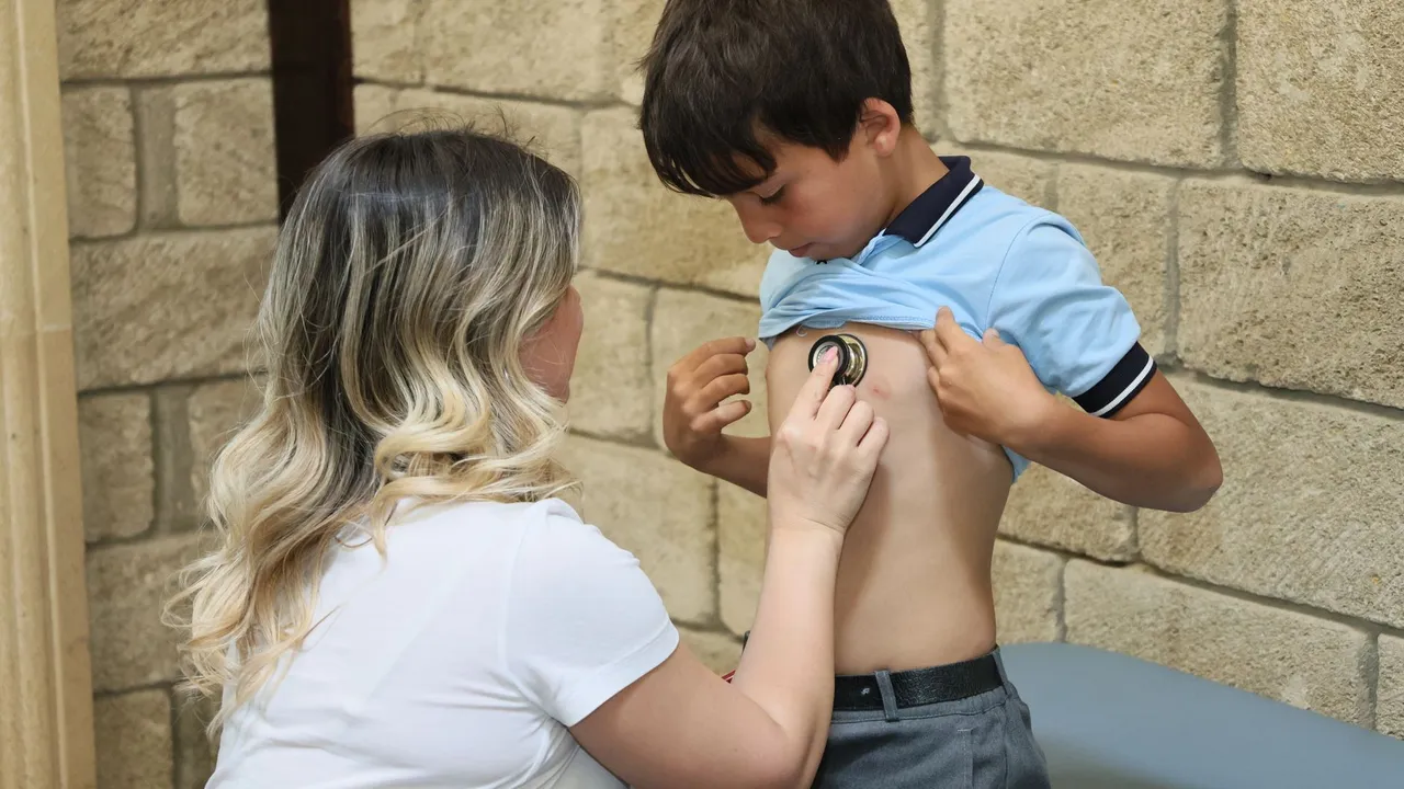 A female doctor uses a stethoscope to listen to a young boy's heartbeat, conducting a health check outdoors.