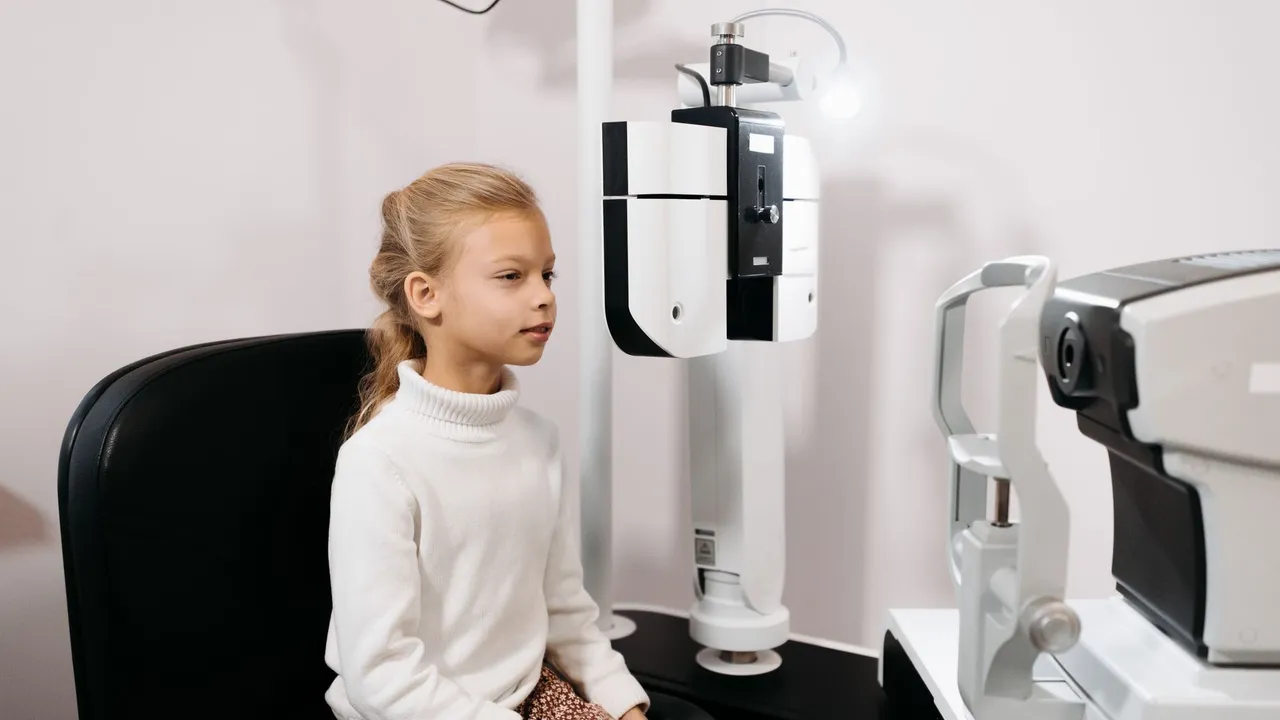 A young girl sits for an eye test using optical instruments in a medical facility.