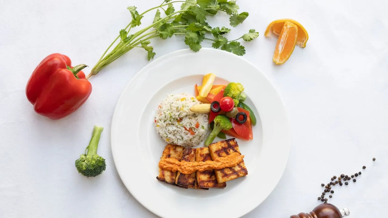 A vibrant and healthy vegan meal featuring grilled tofu, colorful vegetables, and rice served on a white plate.