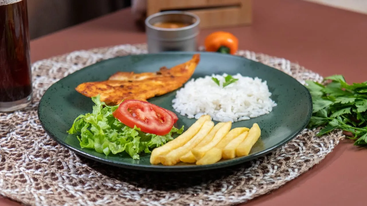 Appetizing meal featuring grilled fish, rice, and fries with fresh salad on a woven mat.