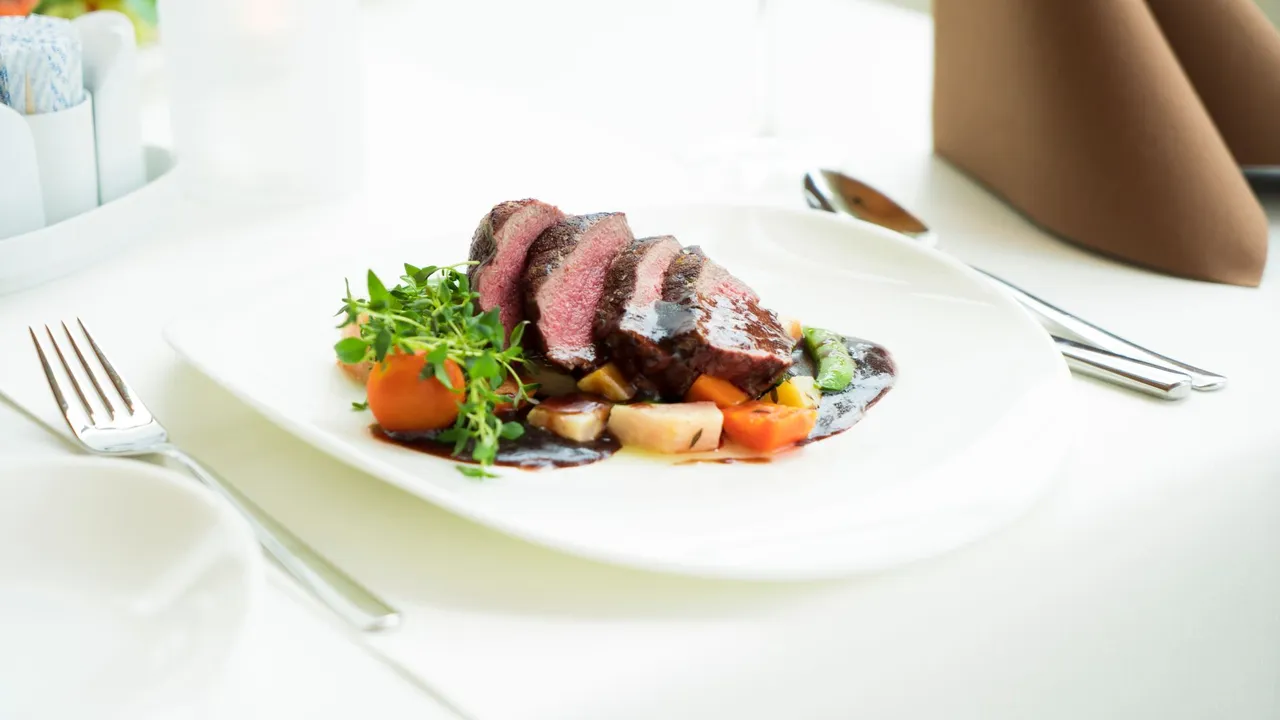 A beautifully presented beef steak with vegetables and sauce in a fine dining setting.