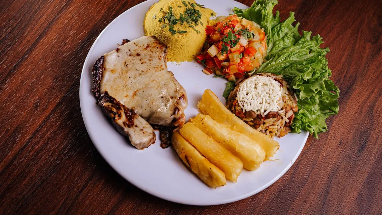 A delicious plate of Brazilian cuisine featuring pork chop, rice, beans, and fresh salad.
