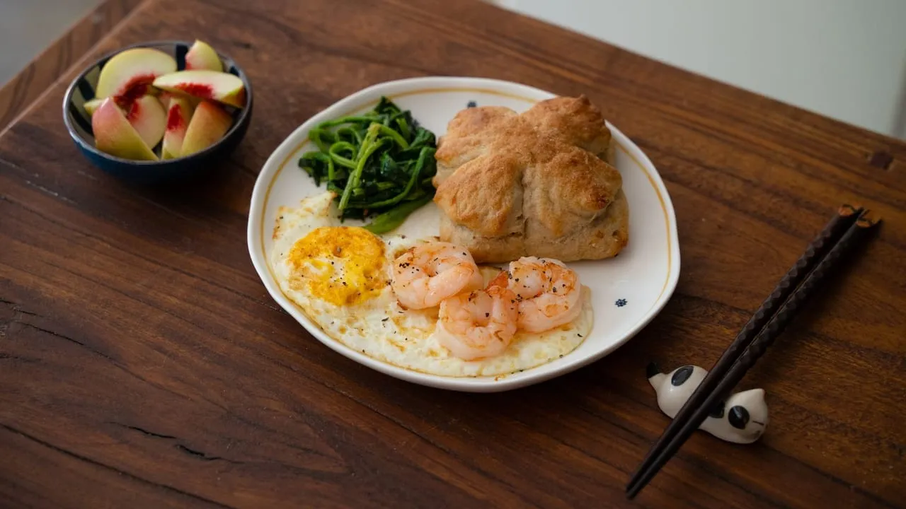 Delicious breakfast featuring shrimps, sautéed greens, biscuit, and fresh peaches.