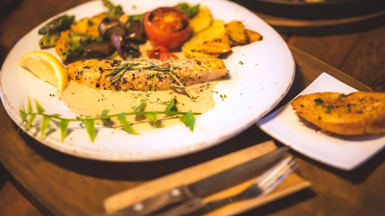 A delicious plated salmon with roasted vegetables, garnished with lemon and herbs on a rustic table.