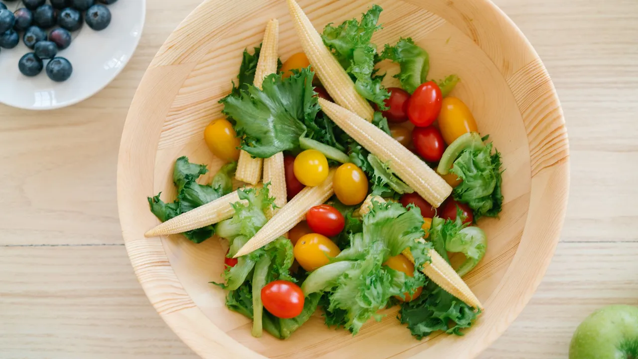 A vibrant salad featuring baby corn, cherry tomatoes, and leafy greens in a wooden bowl, perfect for healthy meals.