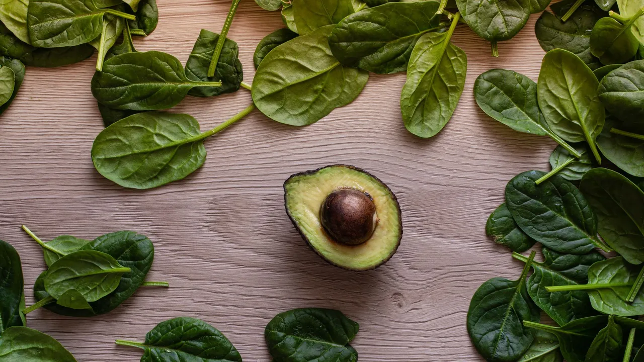 Flatlay of fresh avocado and spinach leaves on a wooden table, perfect for healthy eating concepts.