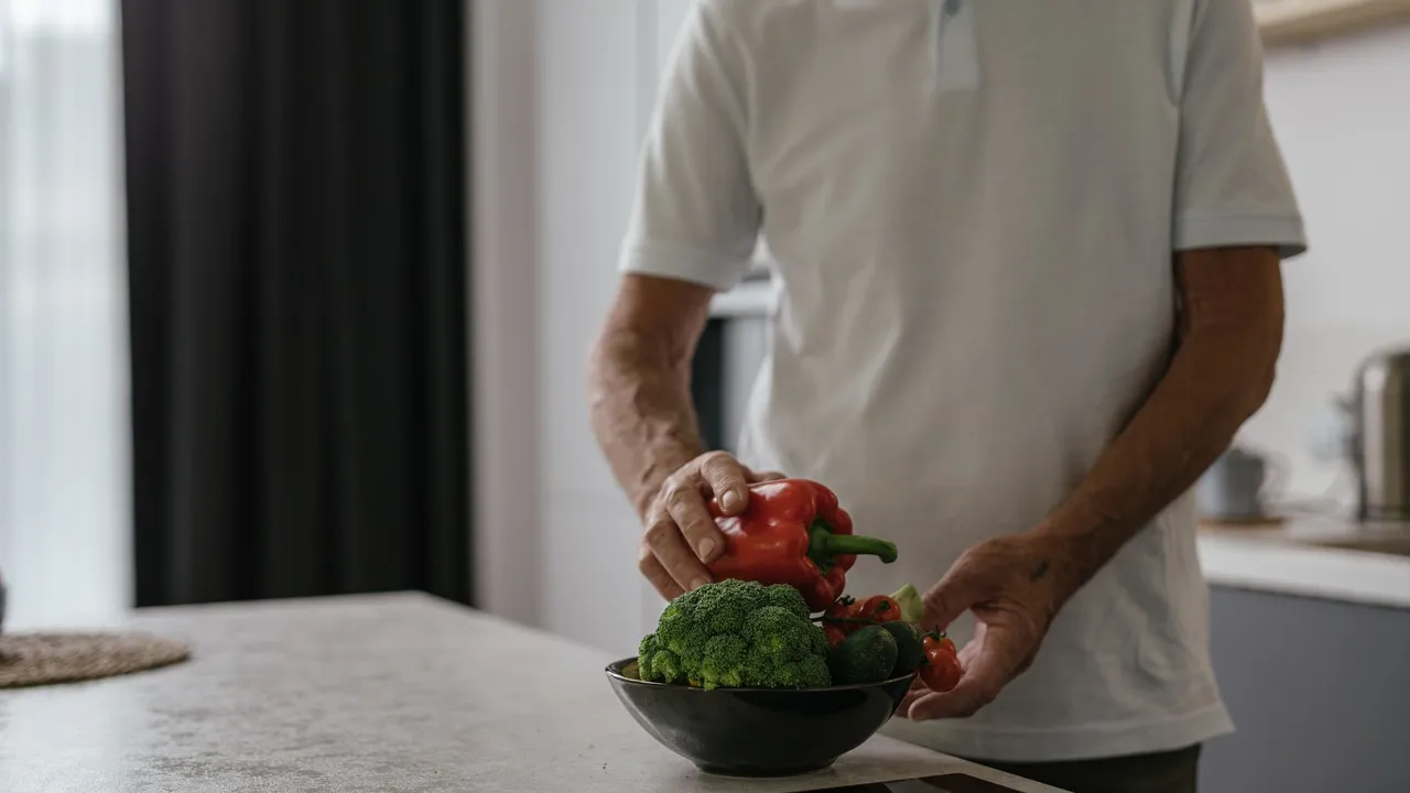Elderly man in kitchen holding vegetables, embracing a healthy lifestyle.