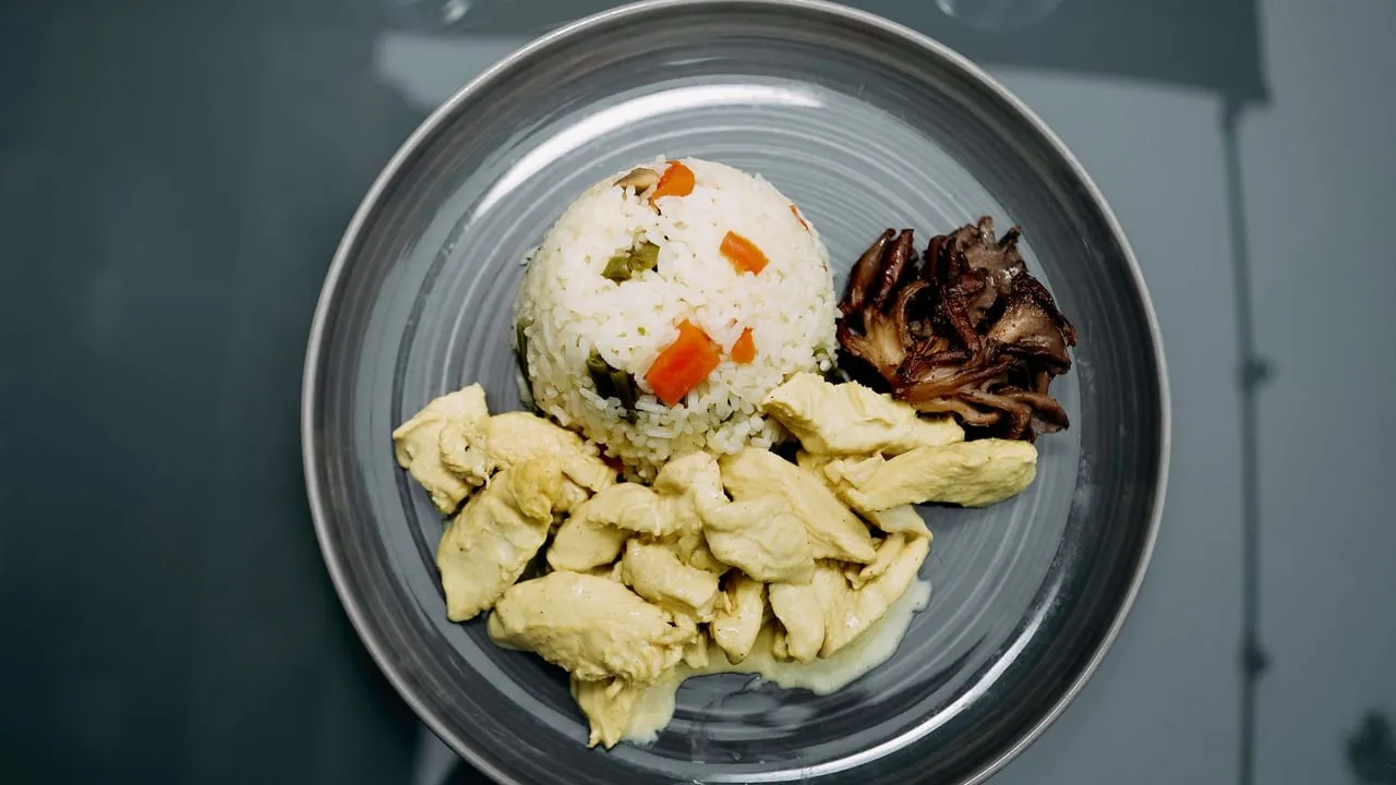A carefully plated meal featuring chicken, vegetable rice, and mushrooms on a ceramic plate.