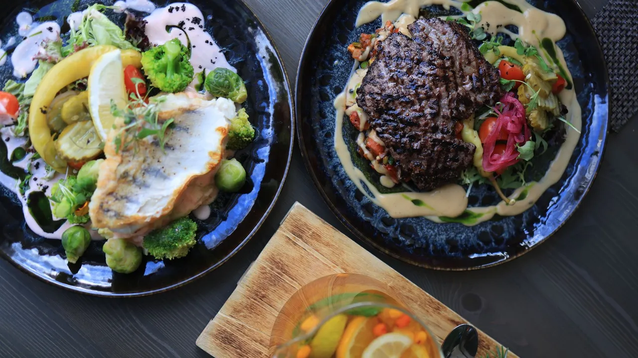 Top view of gourmet fish and steak dishes with fresh citrus and herbs on a stylish table setting.