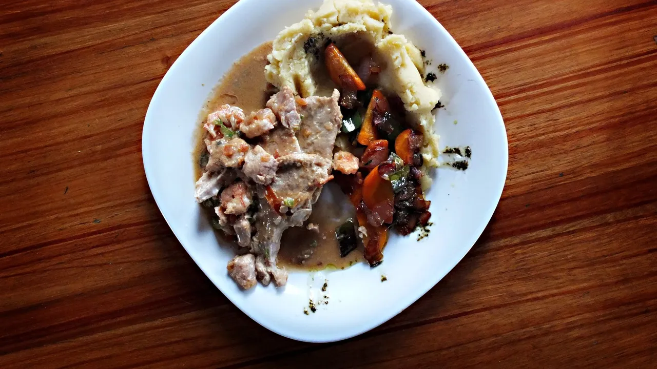 A savory dish of meat and vegetables with mashed potatoes on a wooden table.